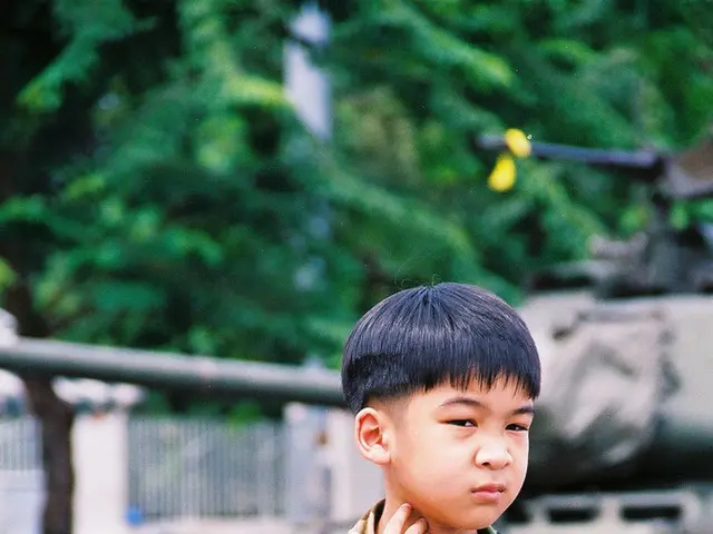 There is a kid sitting on a orange color fencing at the bottom of this image. There is a army...